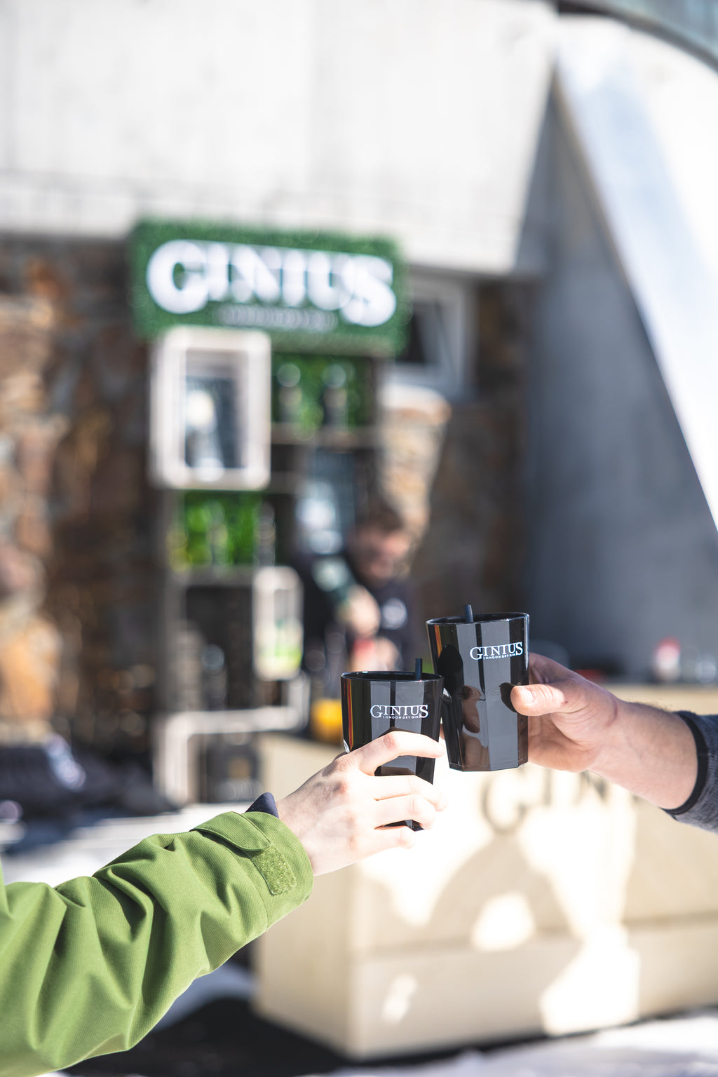 Two people holding cans of GINUS Gin in front of a bar counter with GINUS branding in Winter in the Dolomites.