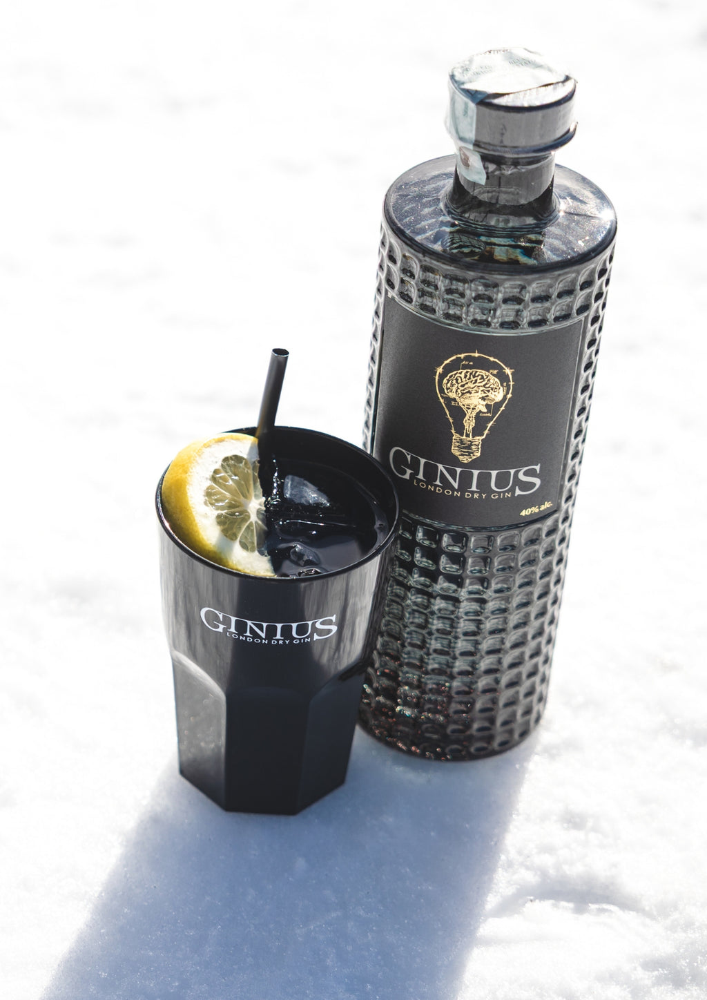Ginius gin bottle and glass (cup) with lemon wedge on a snowy surface