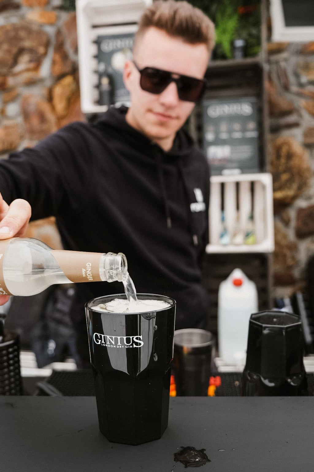 Person pouring a drink into a 'GINIUS' branded cup at a bar.